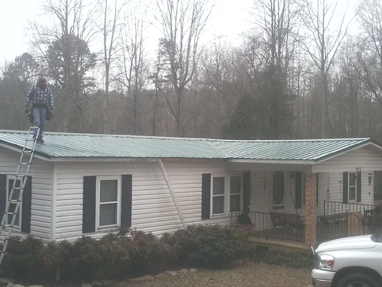 Worker on a ladder beside a new green metal roof on a ranch home in Aliquippa