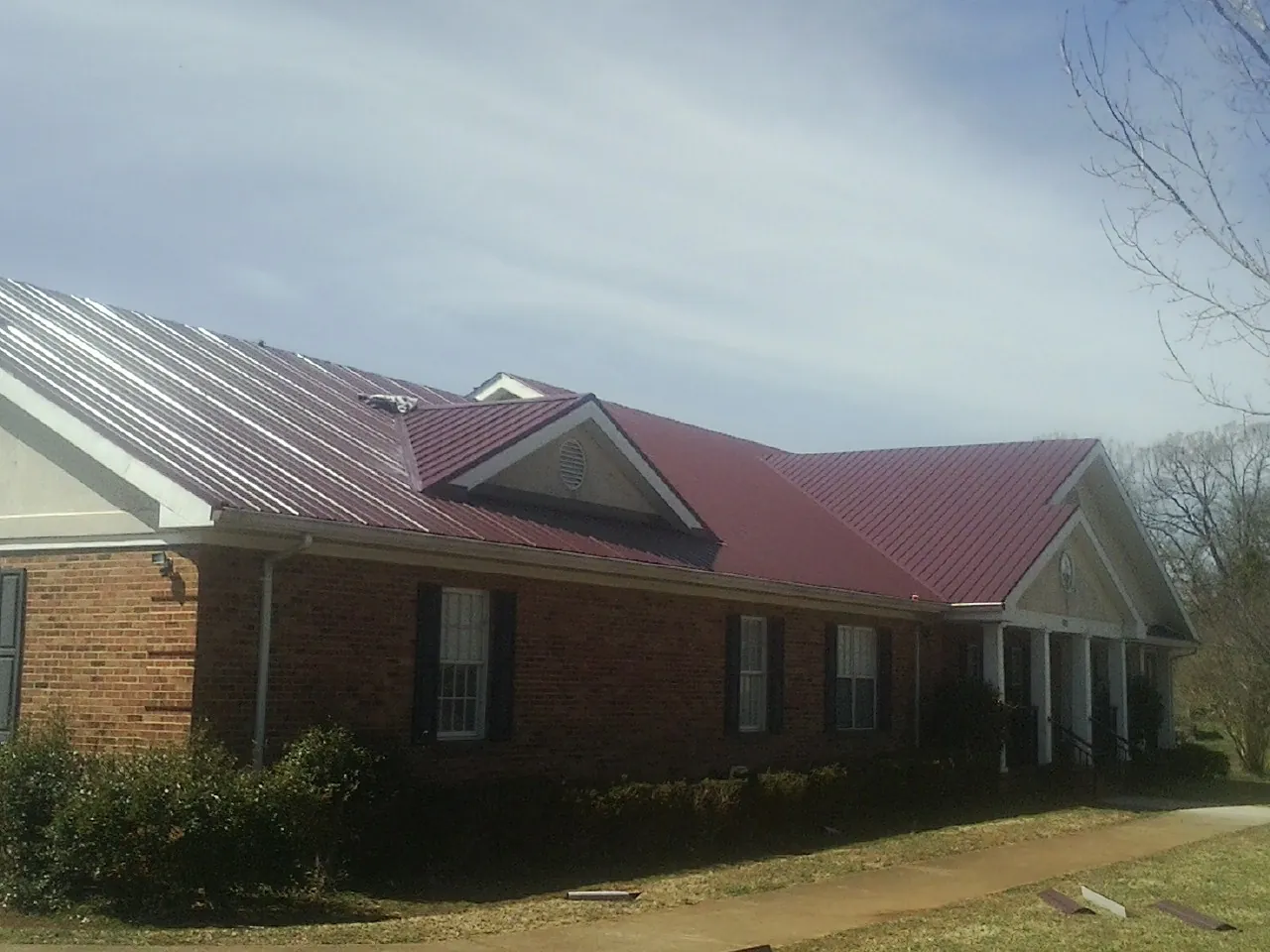 Red metal roof with gabled entries on a long brick building, from a Hail Damage Roof Repair job in Aliquippa