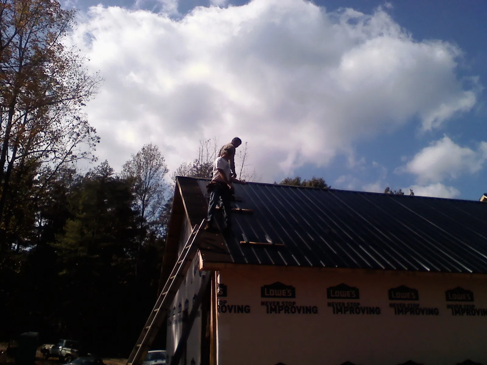 Roofer fastening dark metal panels high against a cloudy sky, from a Roof Inspection job in Aliquippa