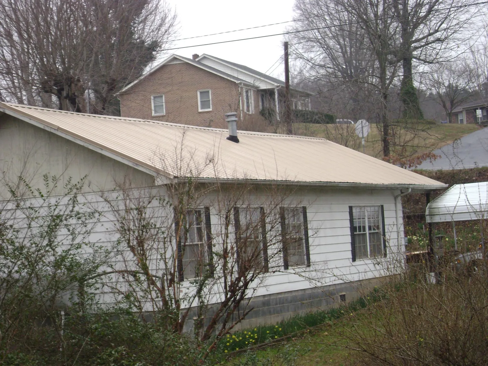 Tan metal roof on a white sided house set into a hillside — Commercial Roofing by Roofing Brothers in Aliquippa